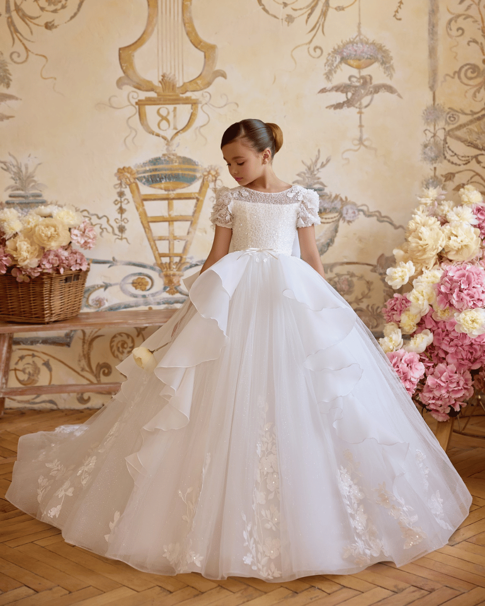 Communiejurk ivoor met gelaagde tule rok en bloemmotieven langs de zoom, elegant en sprookjesachtig.