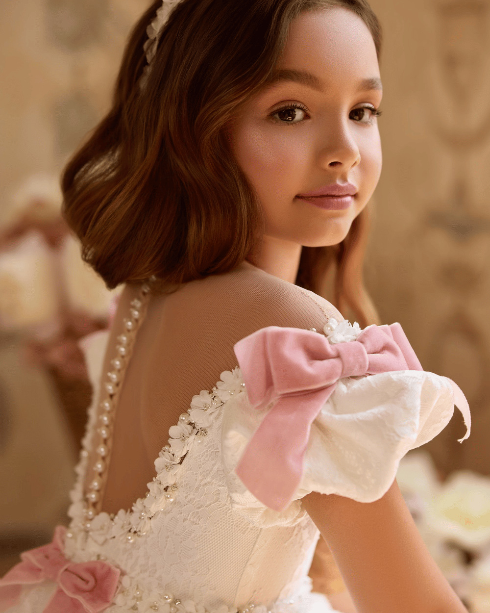 Witte kanten communiejurk met roze strikken en lange sleep uit de So Cute communiejurk winkel