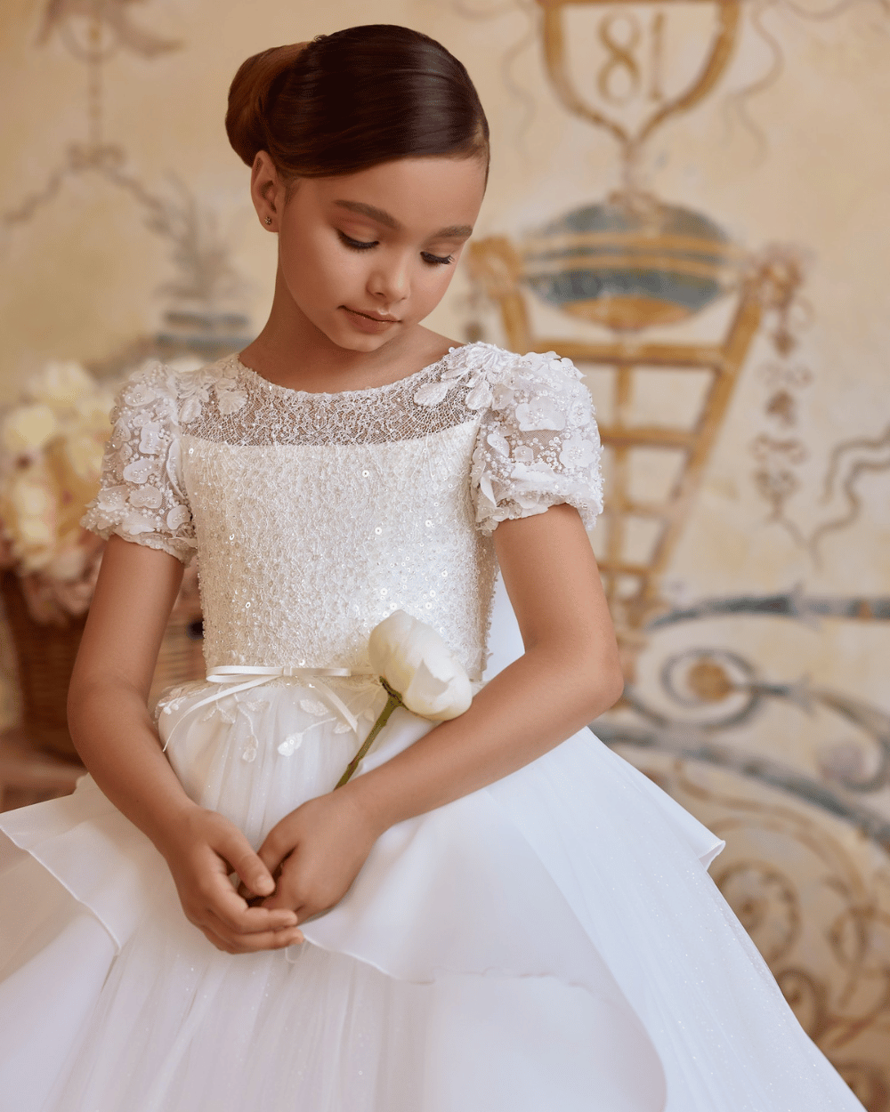 Exclusieve ivoorkleurige communiejurk met lange tule sleep en 3D bloemen, gedragen door een meisje in een klassieke fotosetting